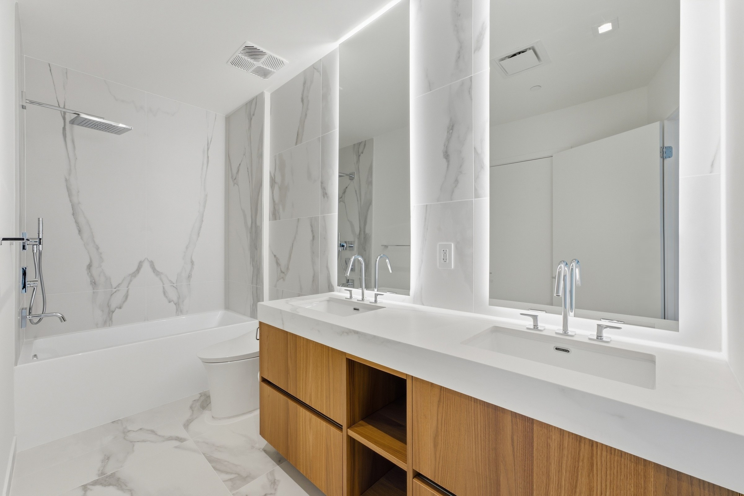Double vanity bathroom with marble-look wall finish and wood cabinetry